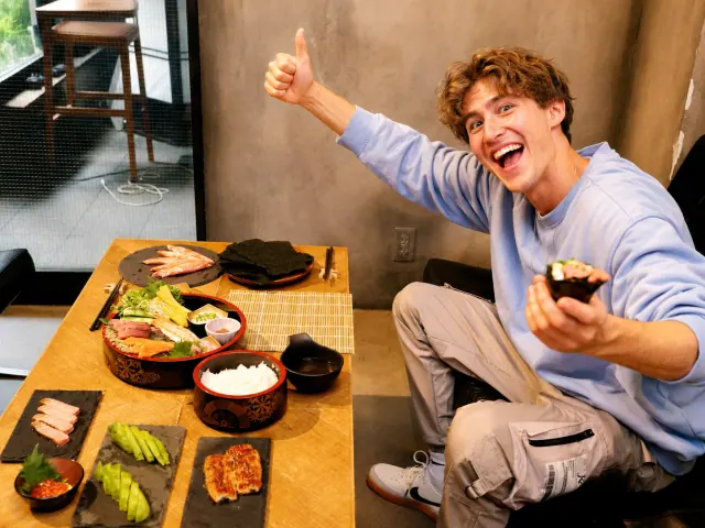 A smiling guest holding a hand roll beside sushi ingredients at Shibuya Sushi Club